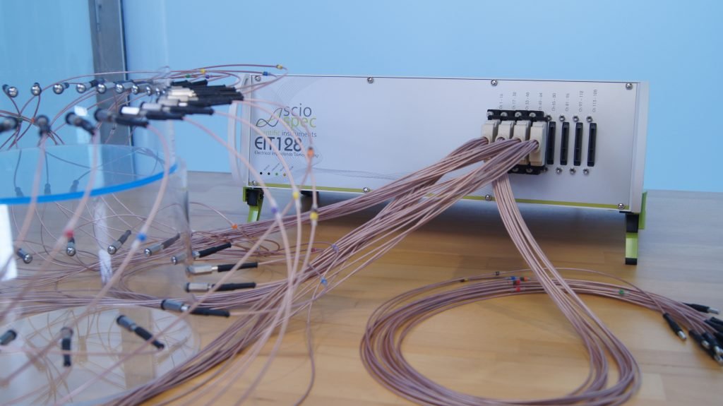 Sciospec EIT128 device connected to a phantom tank, demonstrating scalable EIT imaging from low to high channel counts, adaptable for in-vitro, in-vivo, and clinical research applications.
